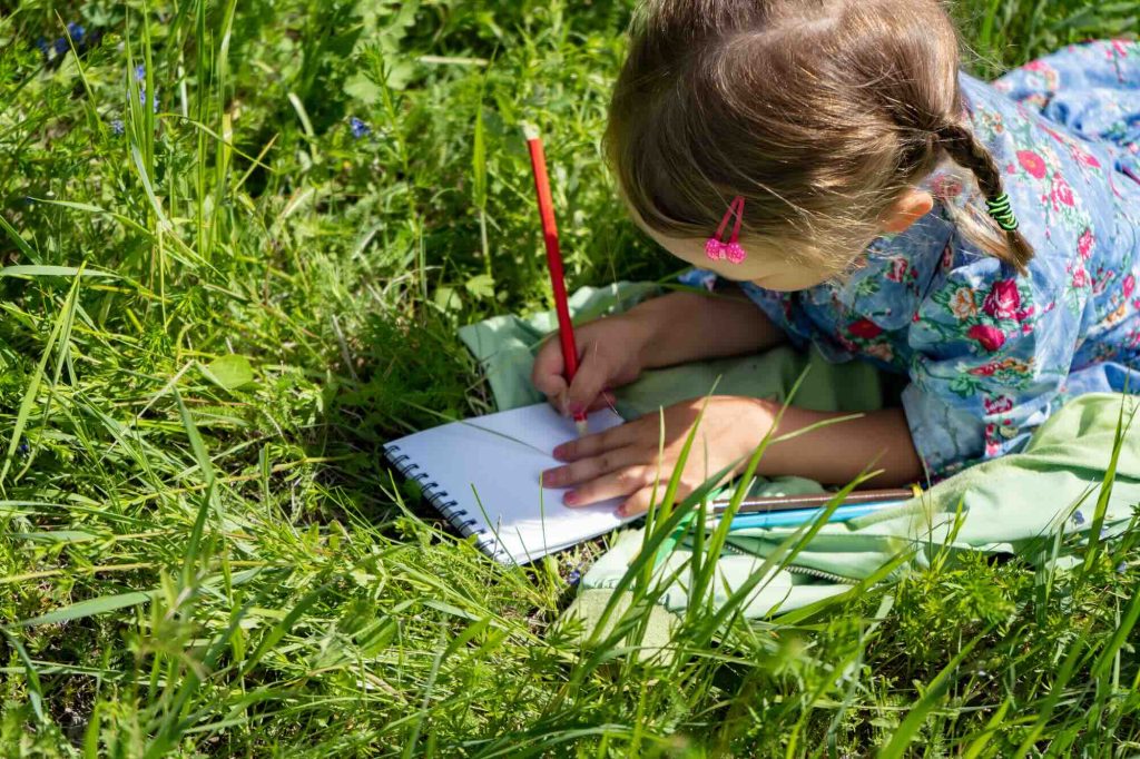 a child drawing in a notebook outdoors